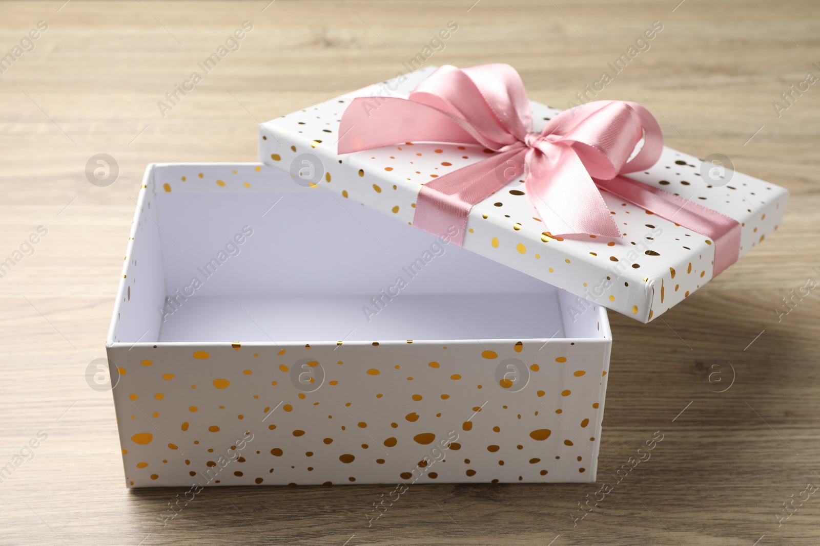 Photo of Opened gift box with beautiful lid on light wooden table, closeup