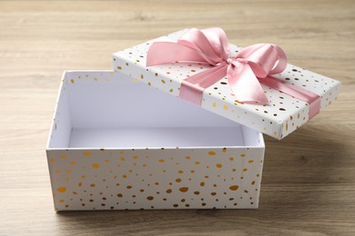 Photo of Opened gift box with beautiful lid on light wooden table, closeup