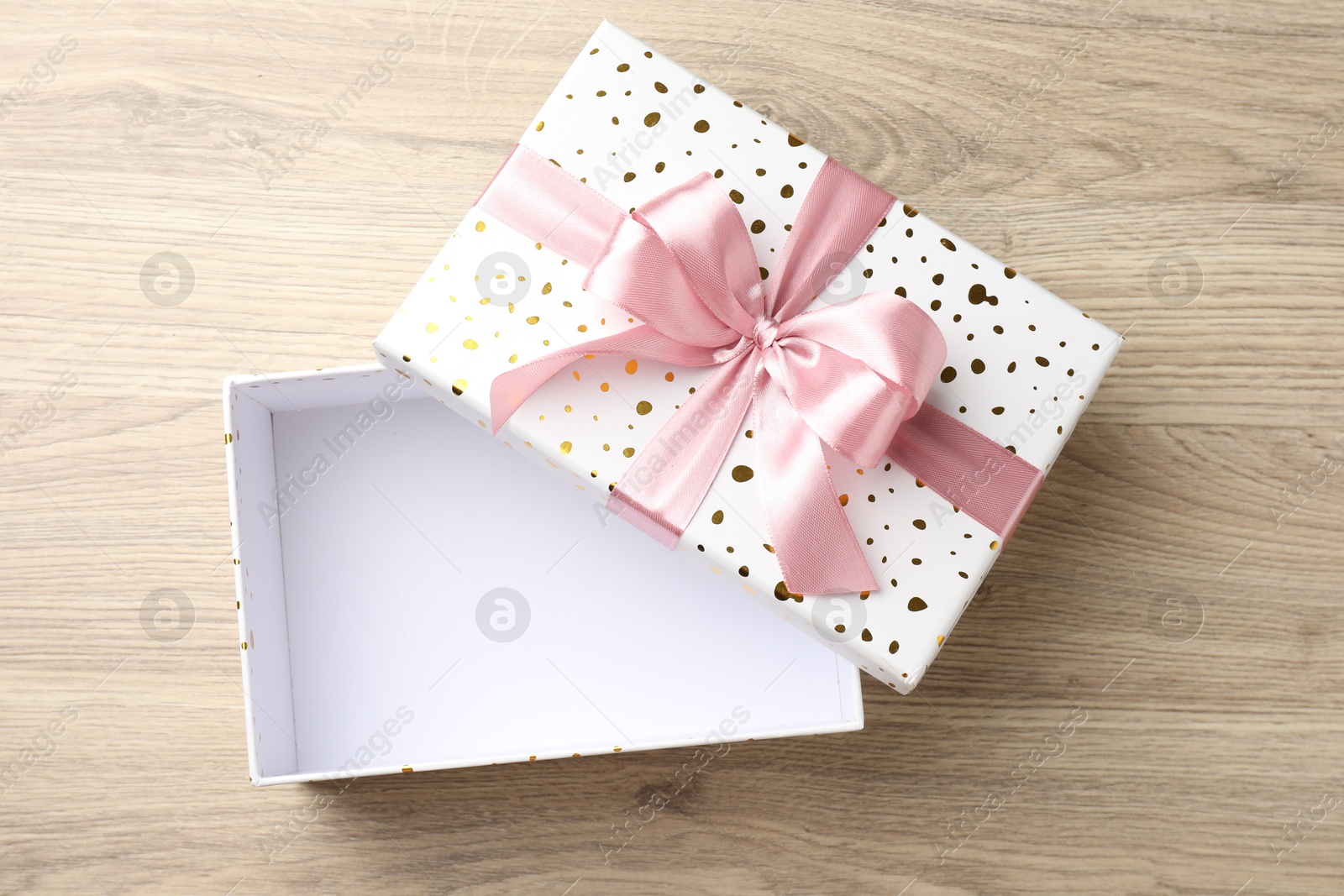 Photo of Opened gift box with beautiful lid on light wooden table, top view