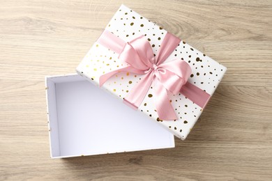 Photo of Opened gift box with beautiful lid on light wooden table, top view