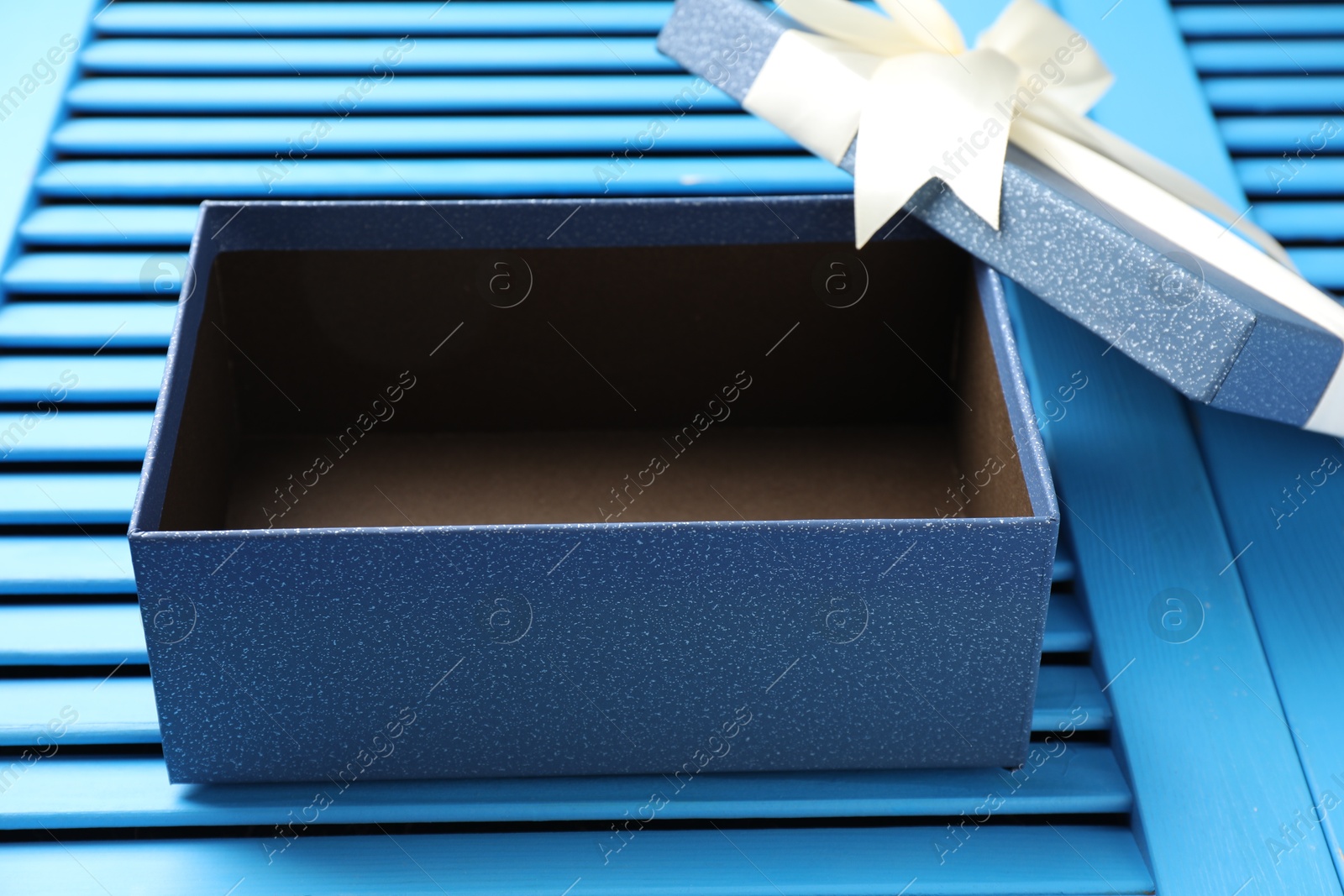 Photo of Opened gift box with beautiful lid on light blue wooden table, closeup