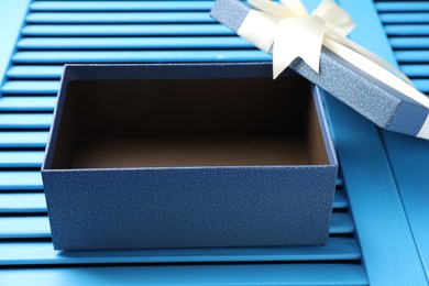 Photo of Opened gift box with beautiful lid on light blue wooden table, closeup
