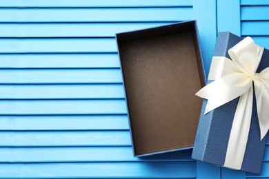 Photo of Opened gift box with beautiful lid on light blue wooden table, top view. Space for text