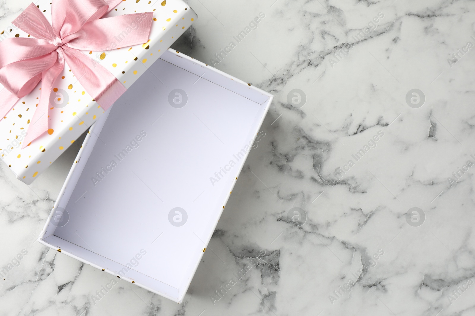 Opened gift box with beautiful lid on white marble table, top view. Space for text Photo of Opened gift box with beautiful lid on white marble table, top view. Space for text