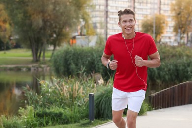 Photo of Happy man in earphones running outdoors, space for text