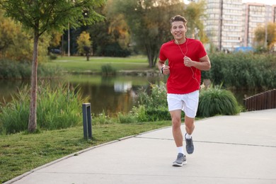 Photo of Happy man in earphones running outdoors, space for text