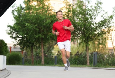 Photo of Happy man in earphones running outdoors, low angle view
