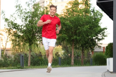 Photo of Happy man in earphones running outdoors, low angle view