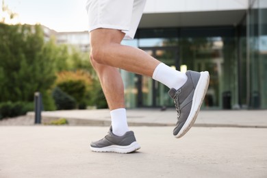 Photo of Athletic man in sneakers running outdoors, closeup