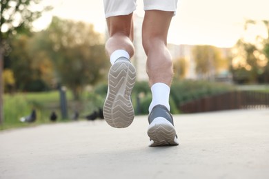 Photo of Athletic man in sneakers running outdoors, closeup