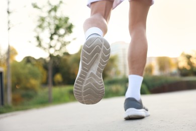 Photo of Athletic man in sneakers running outdoors, closeup