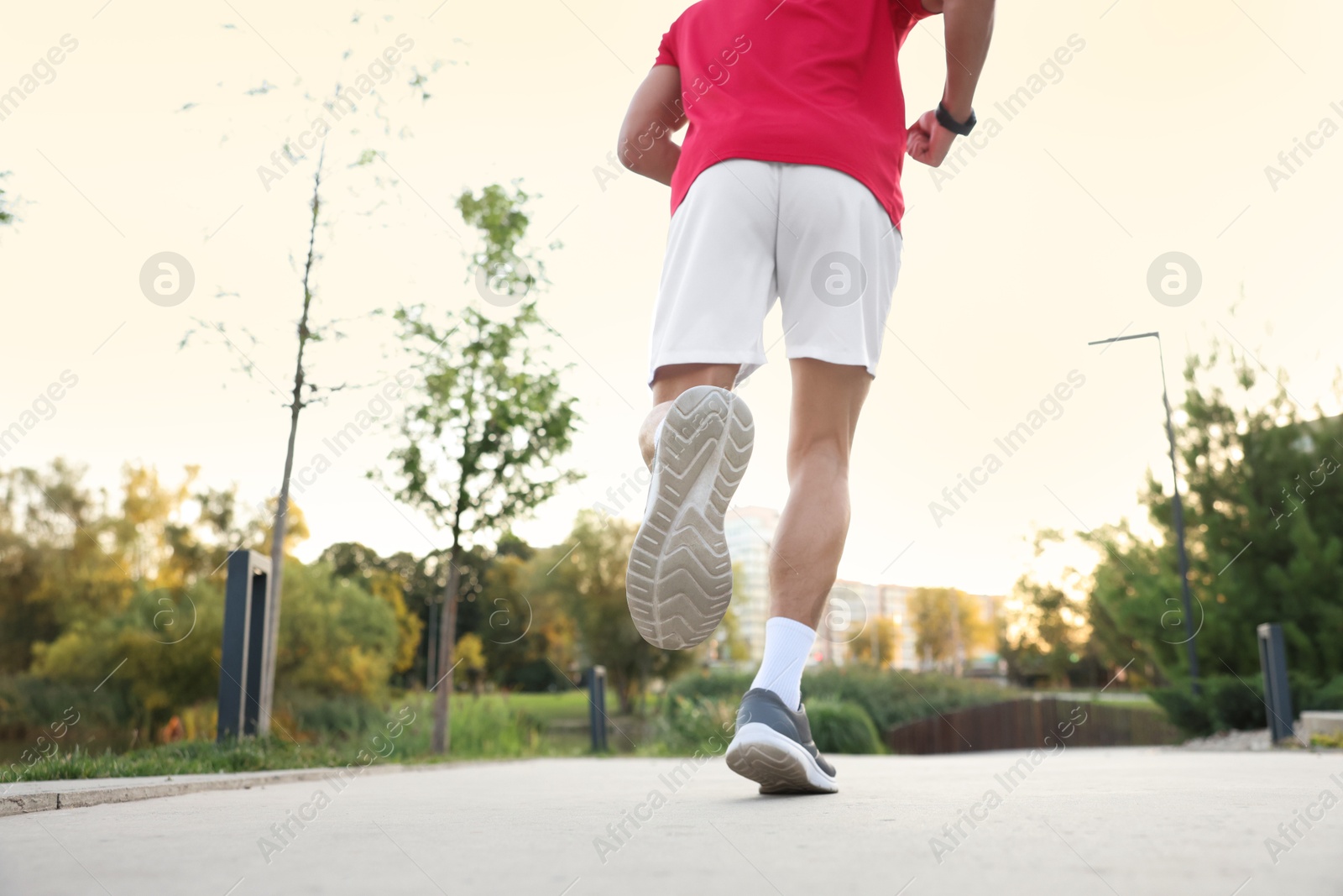 Photo of Athletic man in sneakers running outdoors, back view