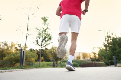 Photo of Athletic man in sneakers running outdoors, back view
