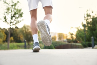 Photo of Athletic man in sneakers running outdoors, closeup