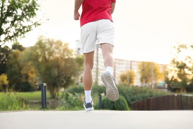 Photo of Athletic man in sneakers running outdoors, back view