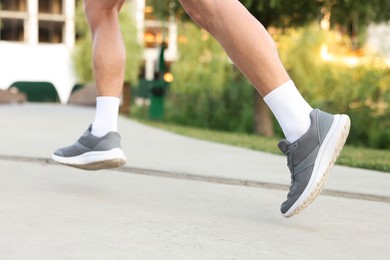 Photo of Athletic man in sneakers running outdoors, closeup