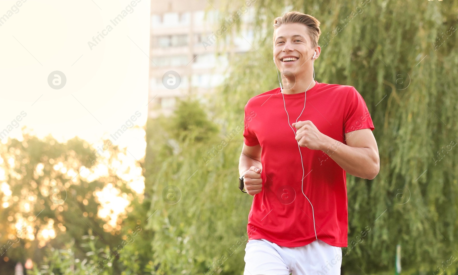 Photo of Happy man in earphones running outdoors, space for text