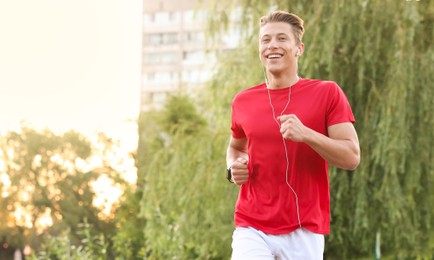 Photo of Happy man in earphones running outdoors, space for text