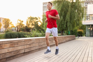 Photo of Happy man in earphones running on city street