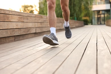 Photo of Athletic man in sneakers running outdoors, closeup