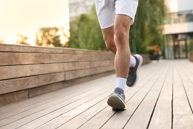 Photo of Athletic man in sneakers running outdoors, closeup