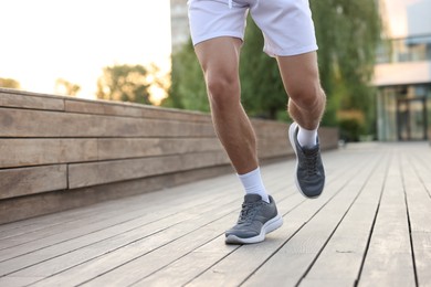Photo of Athletic man in sneakers running outdoors, closeup