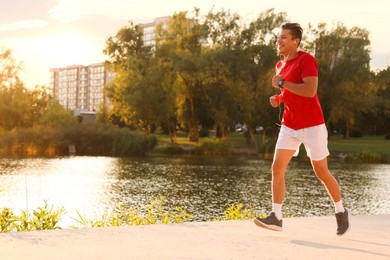Photo of Athletic man running near lake in park, space for text