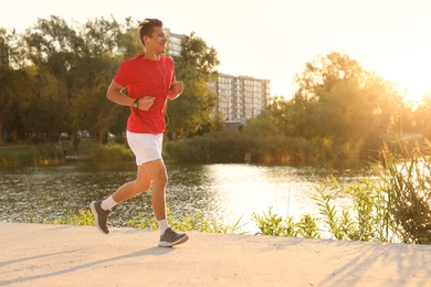 Photo of Athletic man running near lake in park, space for text