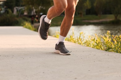 Photo of Athletic man running near lake in park, closeup