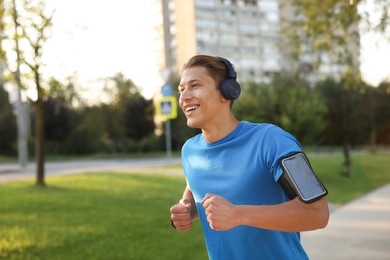 Photo of Happy man with headphones running in park, space for text