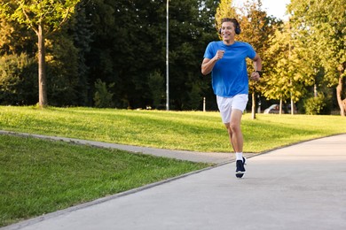 Photo of Happy man with headphones running in park, space for text