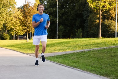 Photo of Happy man with headphones running in park, space for text