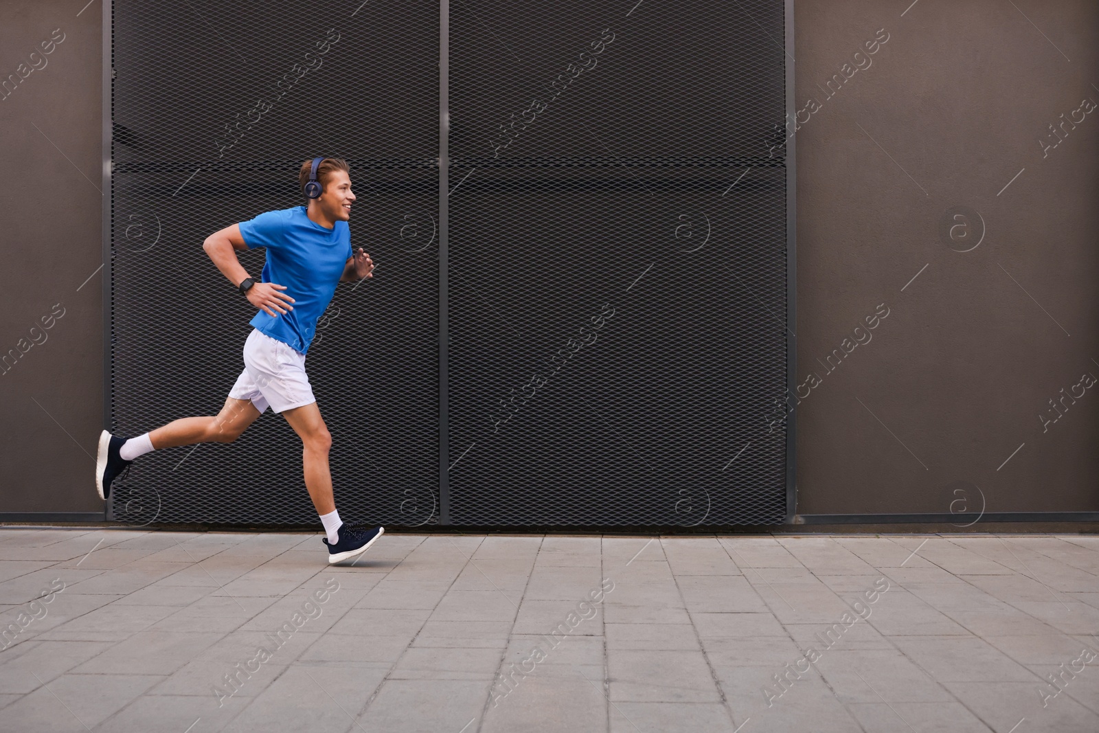 Man in headphones running near building on city street, space for text Photo of Man in headphones running near building on city street, space for text