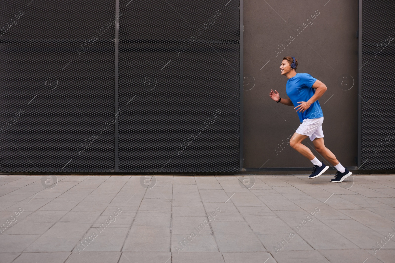 Man in headphones running near building on city street, space for text Photo of Man in headphones running near building on city street, space for text
