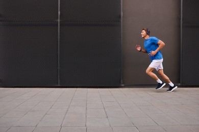 Photo of Man in headphones running near building on city street, space for text