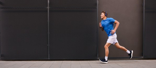 Photo of Man in headphones running near building on city street, space for text