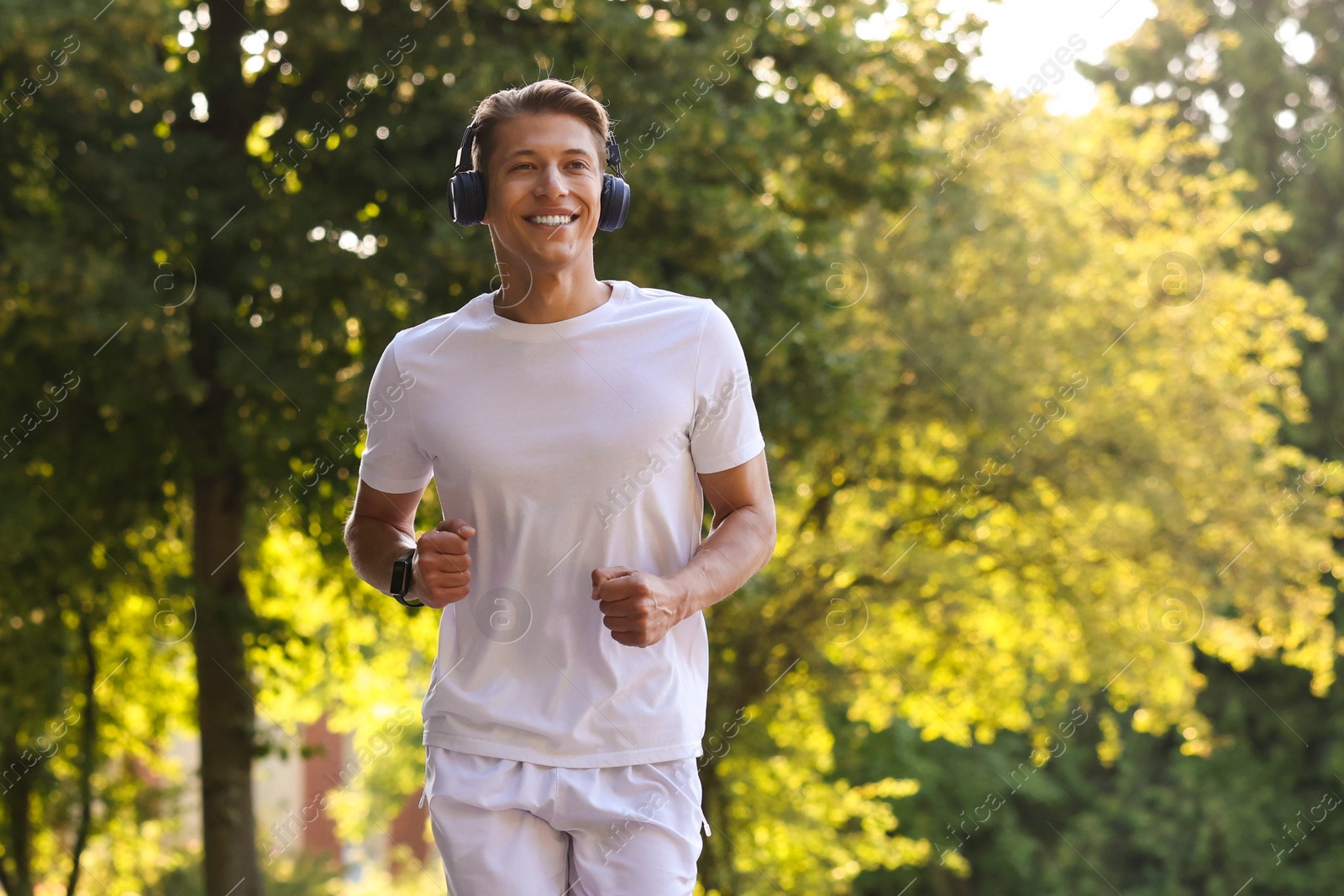 Photo of Happy man with headphones running in park, space for text