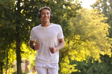 Photo of Happy man with headphones running in park, space for text