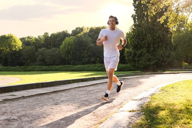 Photo of Happy man with headphones running in park
