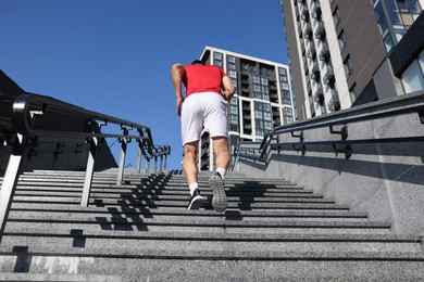 Photo of Man in sportswear running up on stairs outdoors, low angle view