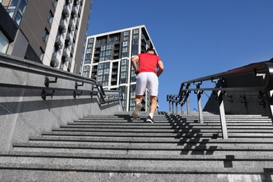 Photo of Man in sportswear running up on stairs outdoors, low angle view