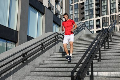 Photo of Man in headphones running down on stairs outdoors