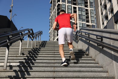 Photo of Man in sportswear running up on stairs outdoors, low angle view
