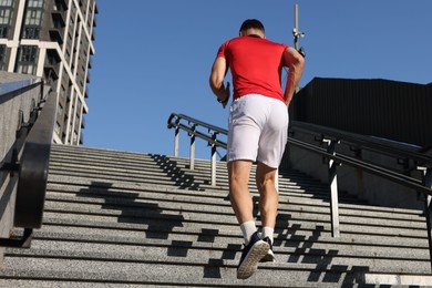 Photo of Man in sportswear running up on stairs outdoors, low angle view. Space for text