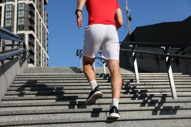 Photo of Man in sportswear running up on stairs outdoors, low angle view