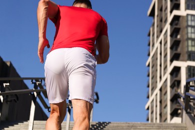 Photo of Man in sportswear running up on stairs outdoors, low angle view. Space for text
