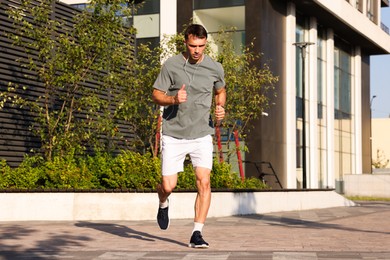Photo of Man in earphones running outdoors on sunny day