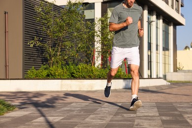 Photo of Man in earphones running outdoors on sunny day, closeup. Space for text