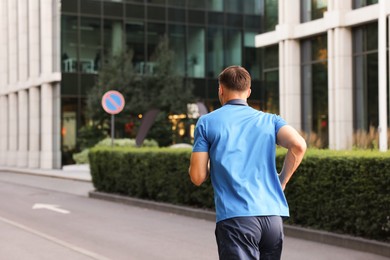 Photo of Man in sportswear running outdoors, back view