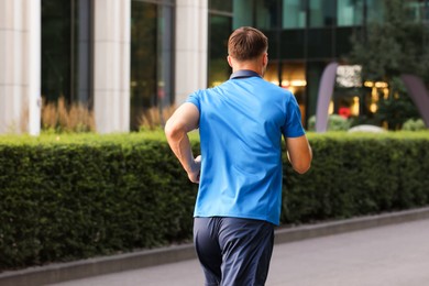 Photo of Man in sportswear running outdoors, back view